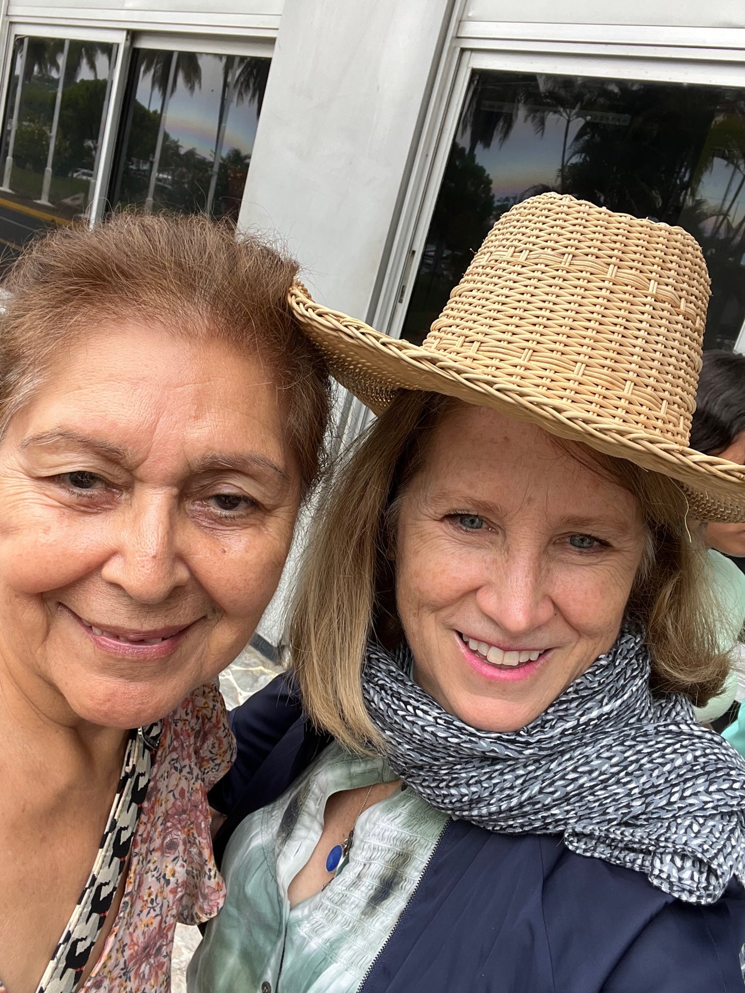 Two women, one donning a straw hat, both pose happily for a photograph, showcasing their joyful expressions.