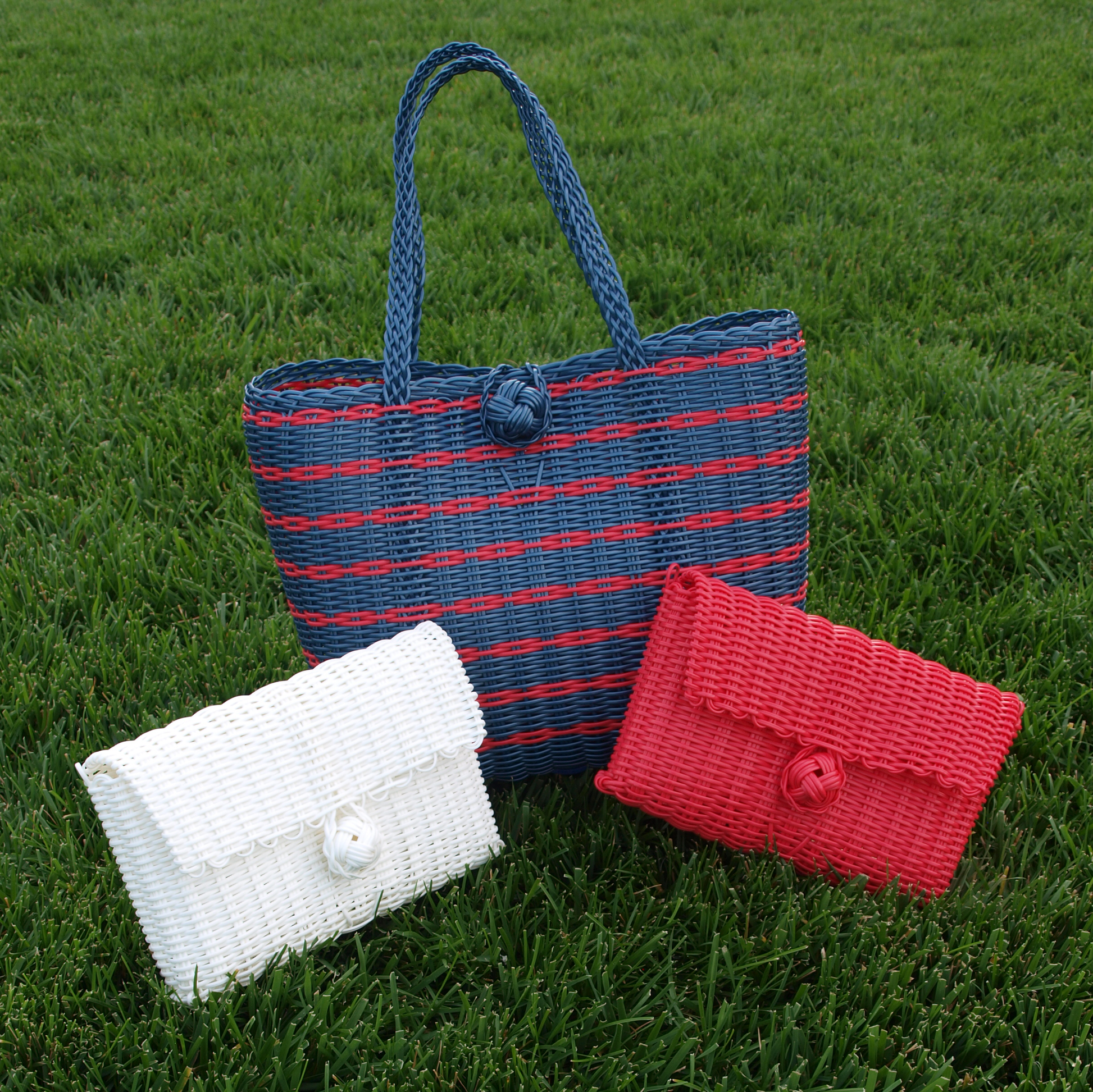 Three woven bags in blue, white, and red on grass