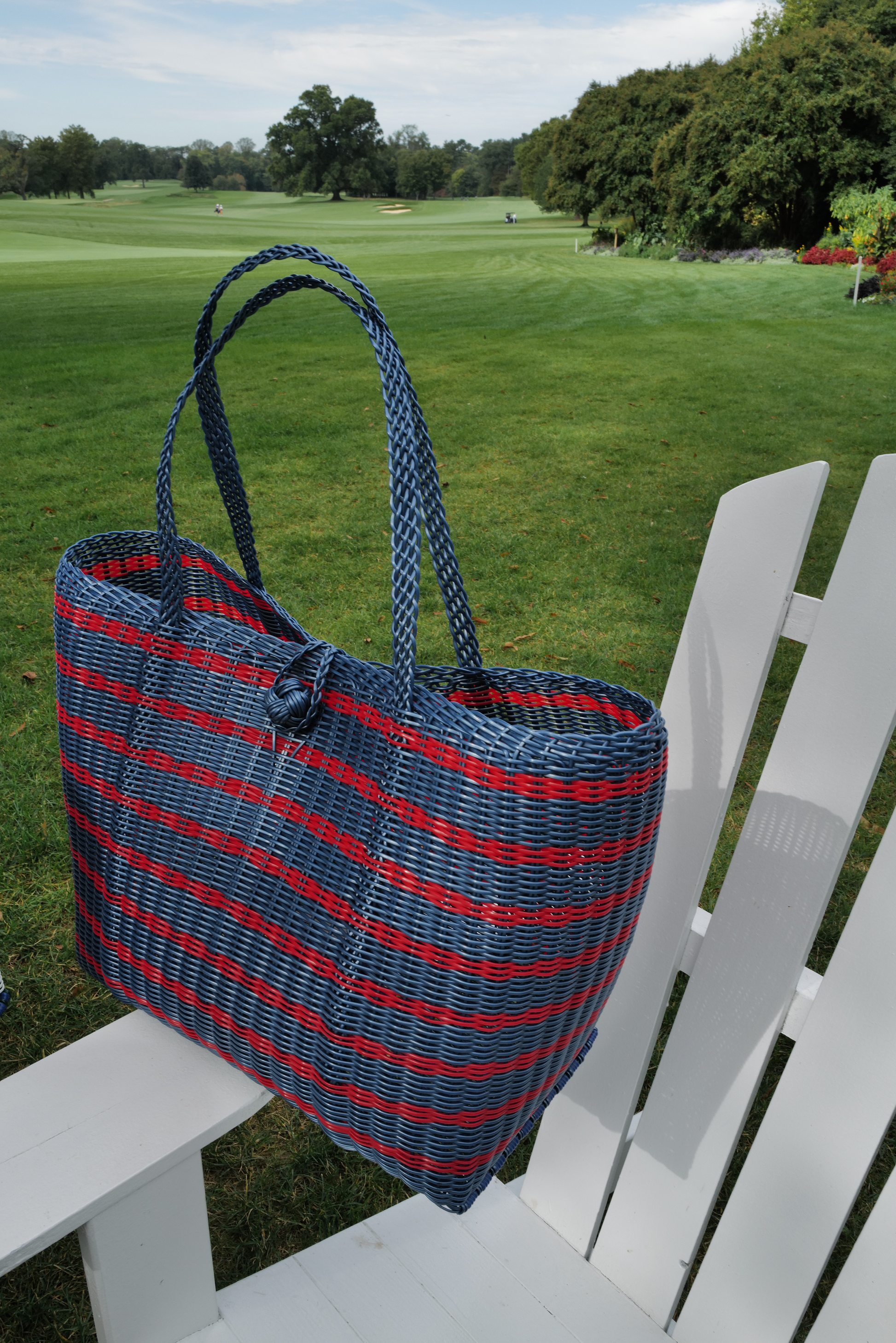 Blue and red striped tote bag on a white chair with a golf course in the background