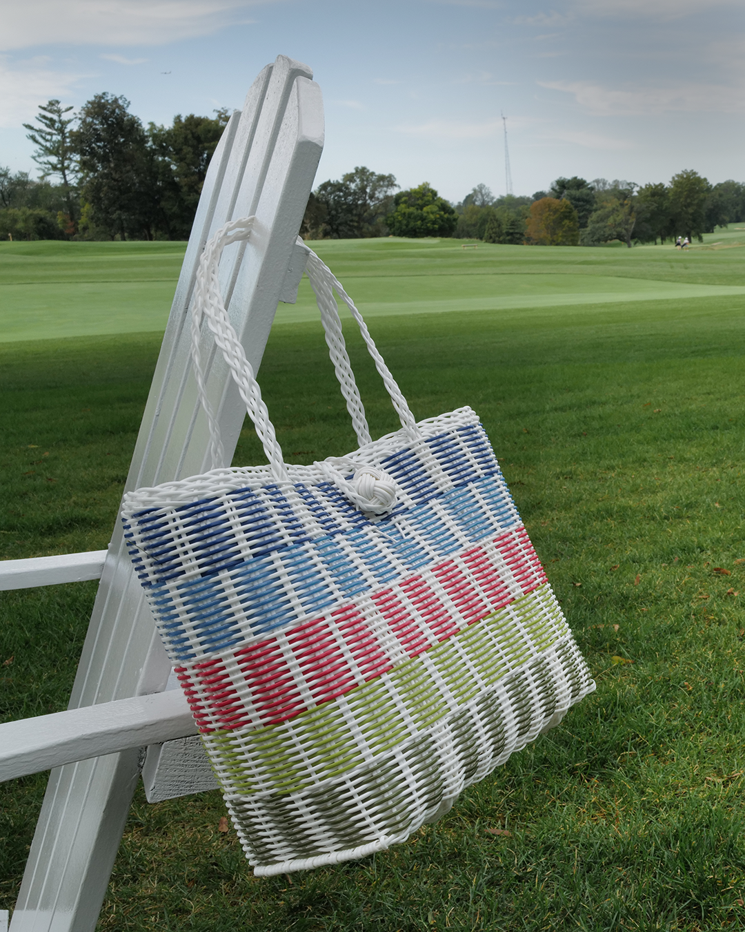 Colorful woven bag on a white chair in a grassy outdoor setting