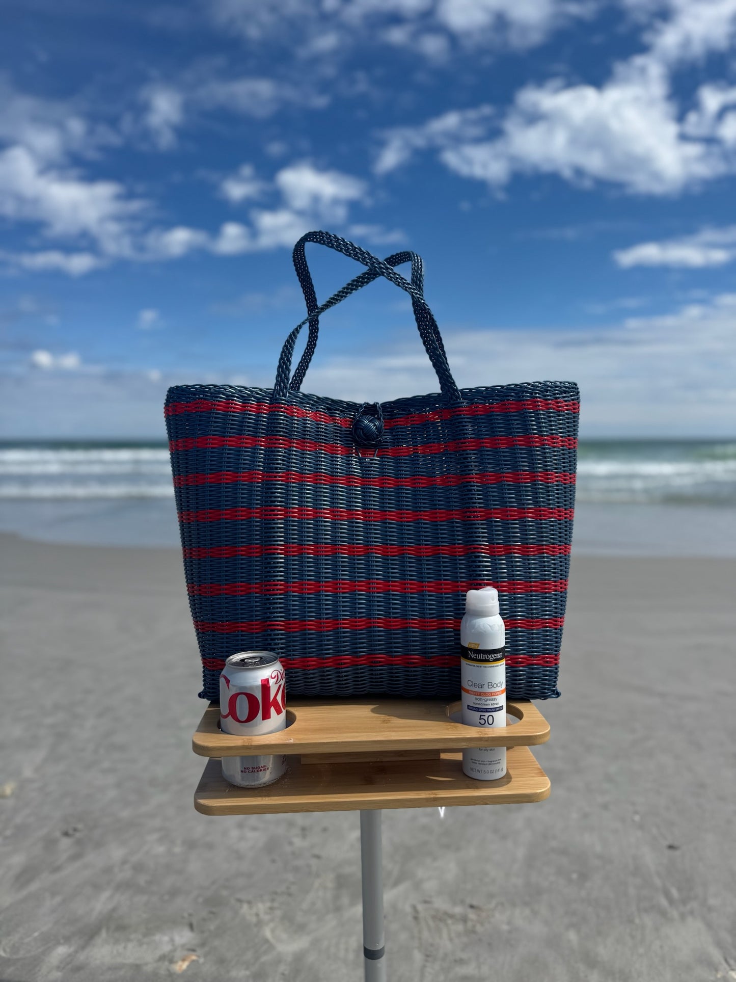 Blue and red striped beach bag with a small wooden table on a sandy beach.
