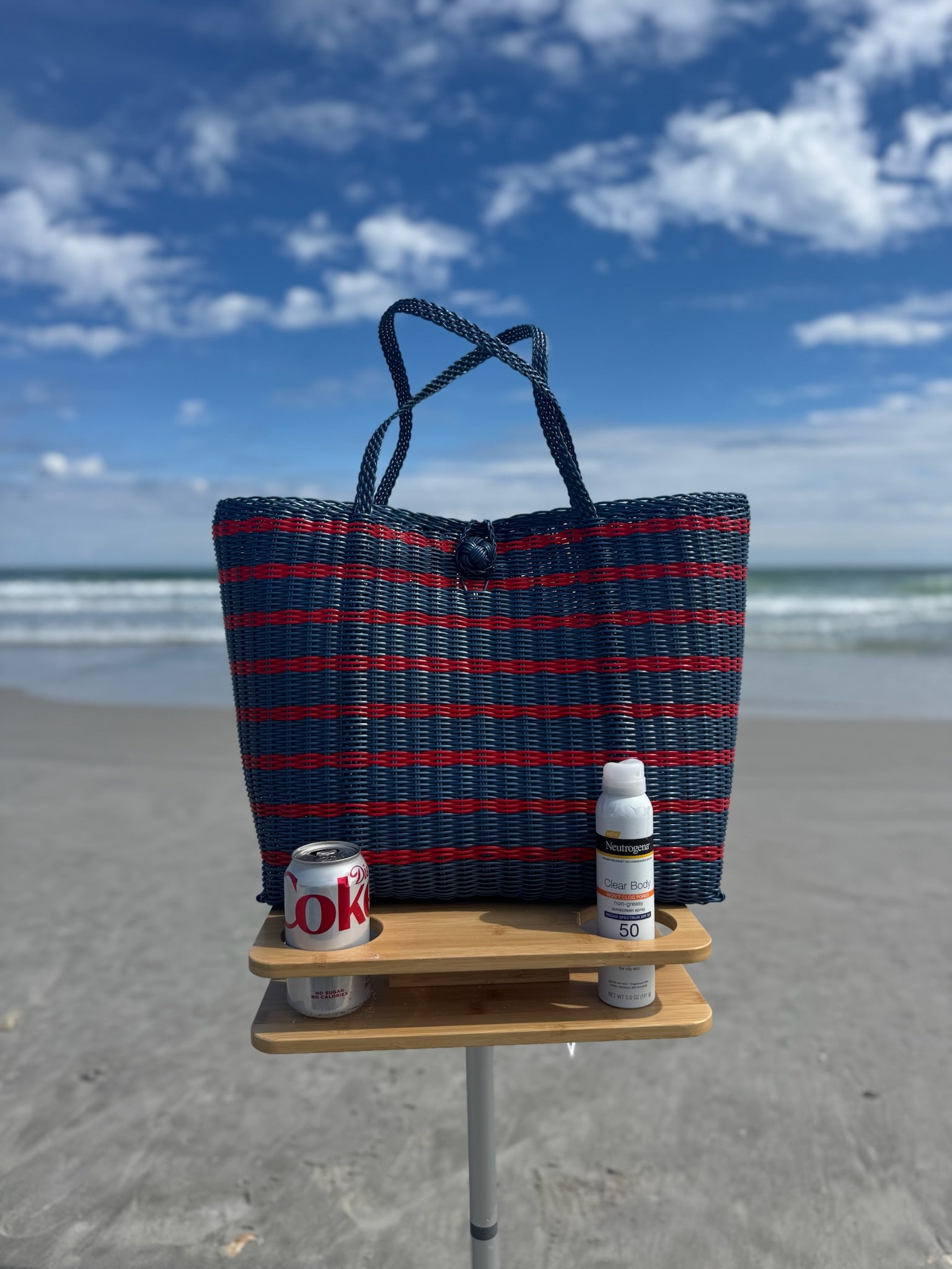 Blue and red striped beach bag with a small wooden table on a sandy beach.